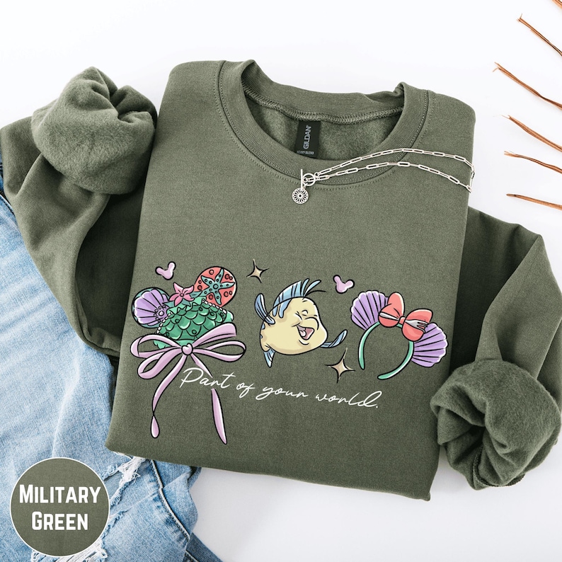 A military green sweatshirt with a graphic design featuring a cartoon fish and flowers, along with the text "Part of your world" printed on it.