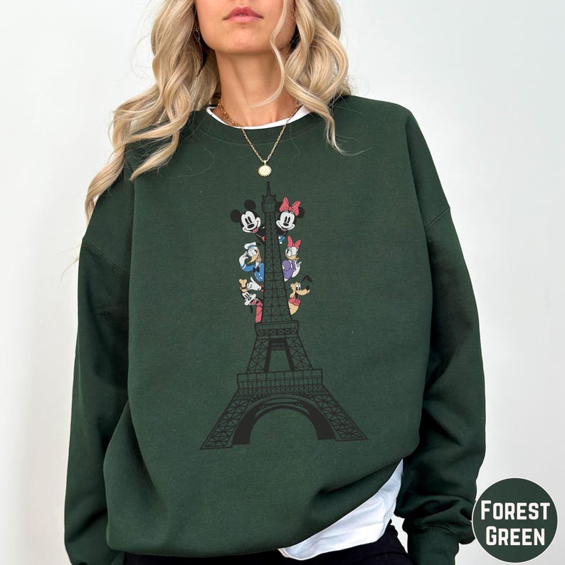 A woman wearing a green sweatshirt with a graphic of the Eiffel Tower and Disney characters on it.