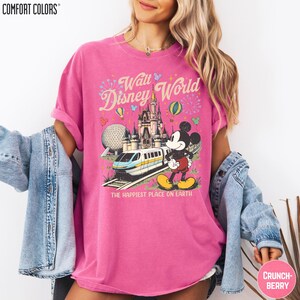 A woman wearing a pink t-shirt with a Disney World graphic and text, along with a denim jacket and a palm frond.