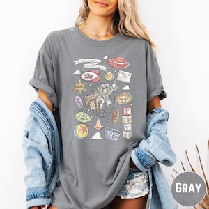 A woman wearing a gray t-shirt with various cartoon characters and icons printed on it, along with a denim jacket.