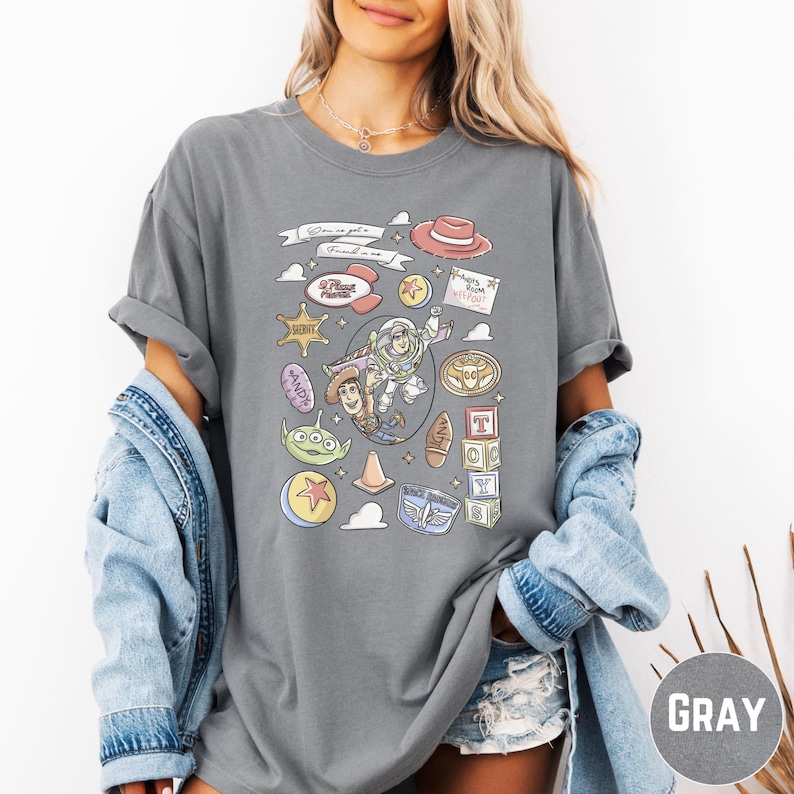 A woman wearing a gray t-shirt with various cartoon characters and icons printed on it, along with a denim jacket.