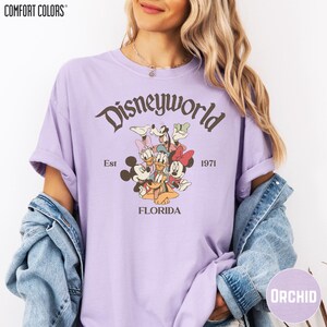 A woman wearing a purple t-shirt with a Disney World logo and text, along with a denim jacket.