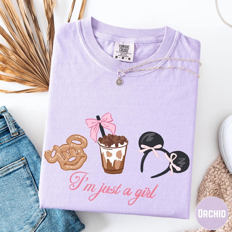 a purple t-shirt with a graphic design of a cup of coffee, a pair of earrings, and a cookie, along with the text "I'm just a girl".