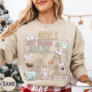 A woman wearing a beige sweater with a Disney-themed graphic and text printed on it.