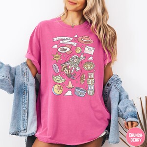 A woman wearing a pink t-shirt with various cartoon characters and icons printed on it, along with a denim jacket.