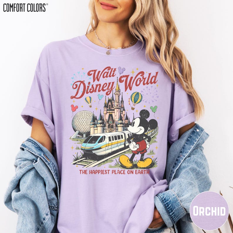 A woman wearing a purple t-shirt with a Disney World graphic and text, along with a denim jacket.