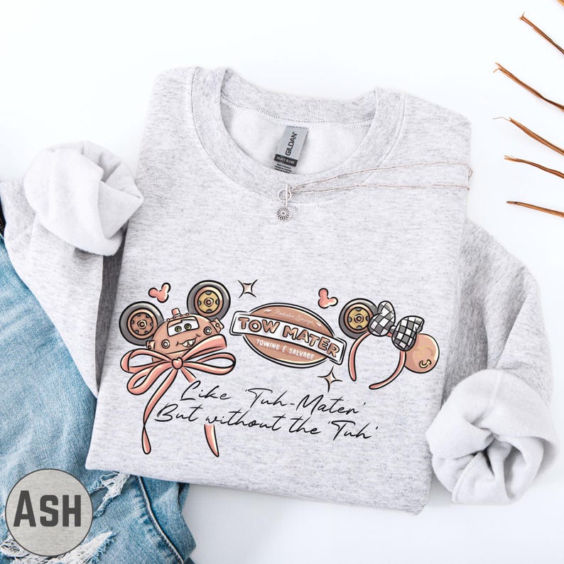 A gray sweatshirt with a graphic design featuring cartoon-style characters and text, along with a necklace and a pair of jeans.