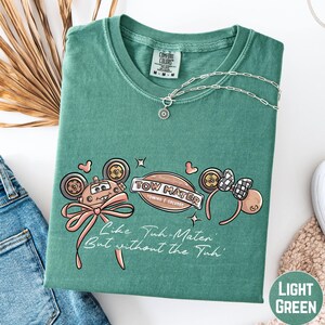 a green t-shirt with a cartoon character design, a necklace, and some other clothing items on a white background.