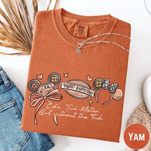 a t-shirt with a cartoon-style design, a necklace, and some accessories, all laid out on a white surface.