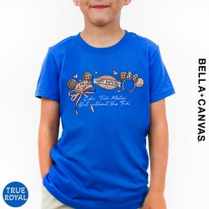 A young boy wearing a blue t-shirt with a Disney-themed graphic and text printed on it.