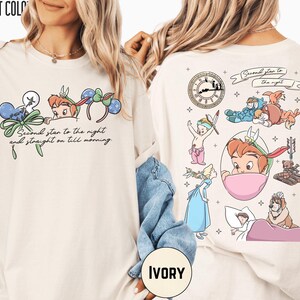 May include: Ivory-colored t-shirt featuring Peter Pan-themed graphics. The front displays Peter Pan and mouse ear headbands with the text "Second star to the night and straight on till morning." The back showcases various Peter Pan characters and elements.