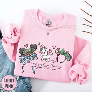A pink sweatshirt with a cartoon character and various Disney-themed items printed on it, along with a necklace and a pair of jeans.