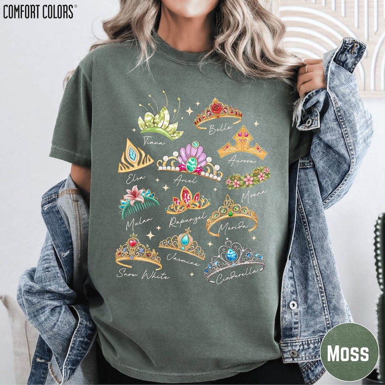 A woman wearing a green t-shirt with a graphic design of various crowns and tiaras, along with the names of the princesses associated with them.