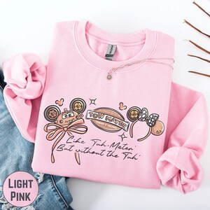 A pink sweatshirt with a cartoon character design and text printed on it, along with a necklace and some twigs.