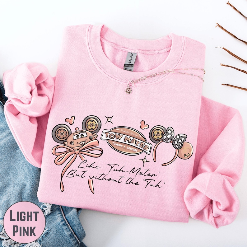 A pink sweatshirt with a cartoon character design and text printed on it, along with a necklace and some twigs.