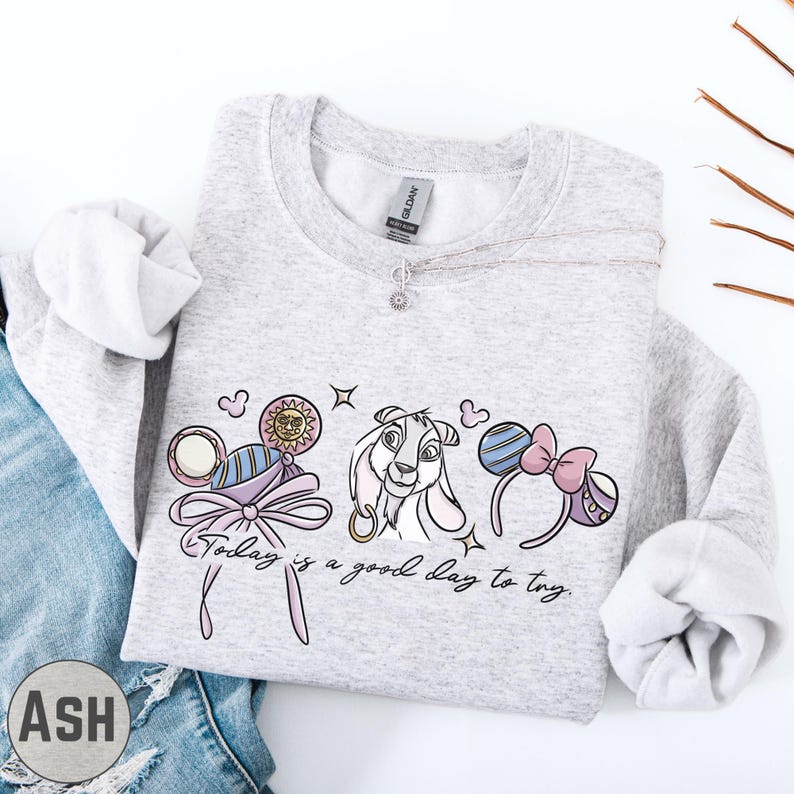A gray sweatshirt with a graphic design featuring a cartoon character and the text "Today is a good day to try" printed on it.