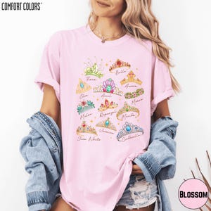 A woman wearing a pink t-shirt with a graphic design of various crowns and tiaras.