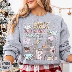 A woman wearing a gray sweatshirt with a graphic design featuring various Disney-themed illustrations and text.