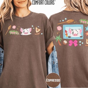a woman wearing a brown t-shirt with a cartoon pig design and various colorful elements, such as a starfish, seashells, and a palm tree.