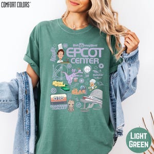 A woman wearing a green t-shirt with various Disney-themed graphics and text, including a chef, roller coaster, and other iconic elements.