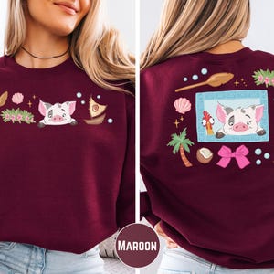 A woman wearing a burgundy sweater with a cartoon pig design and various decorative elements on the back.
