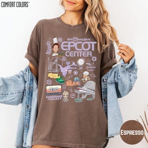 A woman wearing a brown t-shirt with various Disney-themed graphics and text, including characters, landmarks, and other iconic elements associated with the Walt Disney World Epcot Center.