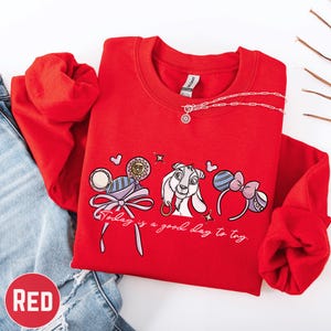 A red sweatshirt with a cartoon character and text printed on it, along with a necklace and a pair of jeans.