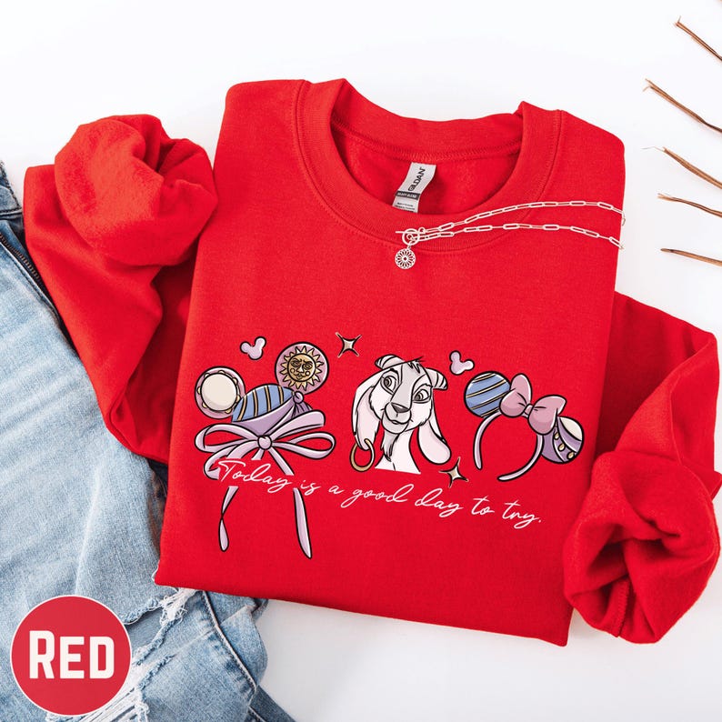 A red sweatshirt with a cartoon character and text printed on it, along with a necklace and a pair of jeans.