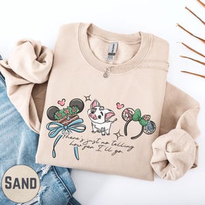 a beige sweatshirt with a cartoon character design, a necklace, and a pair of jeans.