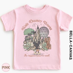 A pink t-shirt with a graphic design depicting various Disney landmarks and characters, including Mickey Mouse and the Eiffel Tower, along with the text "Walt Disney World" and "The happiest place in earth".