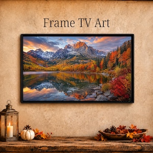 May include: A rectangular digital display framed in black, showing a landscape image of snow-capped mountains, a calm lake, and autumn foliage in shades of orange, red, and yellow. The text Frame TV Art is printed above the display on the wall.