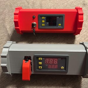 May include: Two rectangular electronic devices, one red and one gray, with digital displays showing numbers. The red device has a key and the gray one has a red switch. Both have a series of buttons and a small screen.