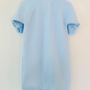 Puede incluir: Saco de dormir para beb&eacute; azul claro con mangas cortas, colgado de una percha blanca. El saco de dormir tiene una textura acanalada y una parte inferior redondeada. El saco de dormir est&aacute; hecho de un material suave.