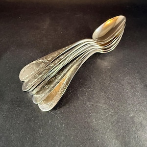 May include: A stack of silver spoons with ornate floral patterns on the handles. The spoons are arranged in a fan shape, with the bowls facing upwards. The spoons are made of a shiny, reflective metal.