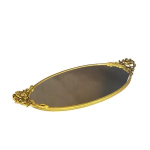 May include: A gold oval-shaped tray with a mirrored surface and ornate floral designs on the sides.