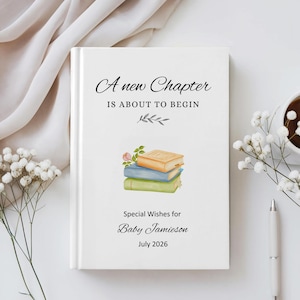 May include: A white book with the text "A new Chapter IS ABOUT TO BEGIN" and "Special Wishes for Baby Jamieson July 2026". The cover features a stack of three books in orange, blue, and green, with a small rose. A pen and a cup of coffee are on the right.