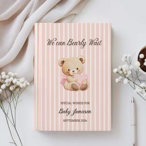 Può includere: Un libro degli ospiti per bambini con una copertina a righe rosa e bianche. La copertina presenta un'illustrazione ad acquerello di un orsacchiotto che tiene un cuore rosa. Il testo recita "We can Bearly Wait" e "Special Wishes for Baby Jamieson September 2026."