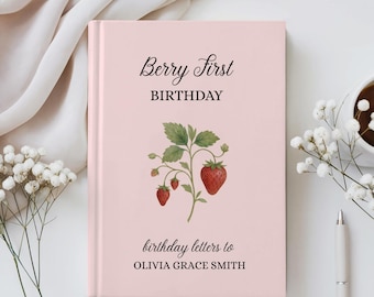 May include: A pink hardcover journal with the text "Berry First Birthday" and "birthday letters to OLIVIA GRACE SMITH." A watercolor illustration of strawberries and leaves is featured on the cover. A pen and a cup of coffee are on the right.