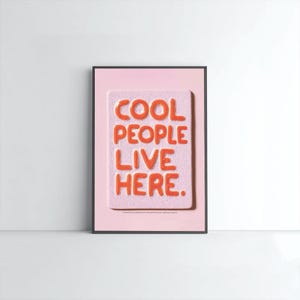 Puede incluir: Impresión artística enmarcada con el texto "COOL PEOPLE LIVE HERE" en naranja sobre fondo rosa. El texto tiene un efecto 3D. El marco es negro y el fondo es blanco.