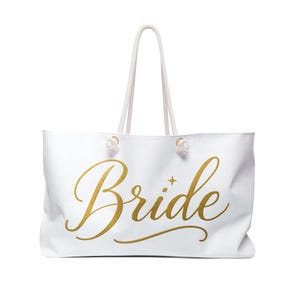 May include: White tote bag with gold script text that reads "Bride". The bag has white rope handles and is designed for carrying items. A star graphic is next to the word "Bride".