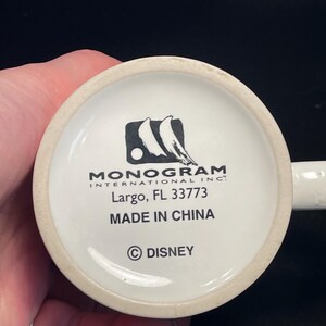 May include: White ceramic mug base with the text "MONOGRAM INTERNATIONAL INC." and "Largo, FL 33773". The text "MADE IN CHINA" and the Disney copyright symbol are also visible.