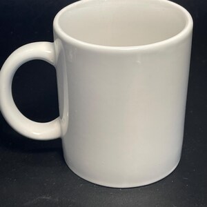 May include: A white ceramic mug with a rounded handle. The mug is cylindrical and has a smooth, glossy finish. The mug is empty and ready to be filled with a beverage.