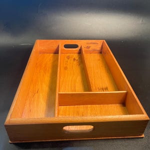 May include: A rectangular wooden tray with a natural light brown finish, featuring three distinct interior compartments separated by fixed dividers and two oval-shaped cutout handles located on the front and back side panels.