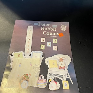 May include: A book titled "Peter Rabbit Counts" with illustrations of Peter Rabbit and other characters. The cover features a variety of images, including a crib, a chair, and a basket, all with a Peter Rabbit theme.