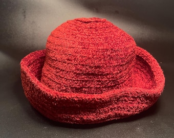 Puede incluir: Un sombrero cloche rojo con una apariencia texturizada y tejida. El sombrero presenta una corona redondeada y un ala inclinada hacia abajo. El sombrero está hecho de un material suave, posiblemente tejido.