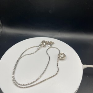 Op de afbeelding: Een zilverkleurige ketting met een fijne ketting. De ketting heeft een ronde hanger met een centrale heldere steen. De ketting is ongeveer 40 cm lang.