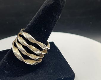 May include: A silver ring with a unique design. The ring features a series of wavy, overlapping bands, creating a textured and eye-catching appearance. The ring is displayed on a black velvet ring holder, showcasing its intricate details.