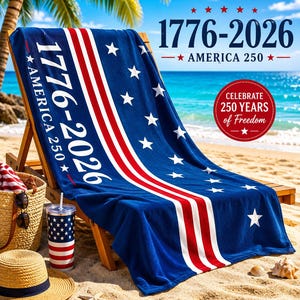May include: A blue beach towel with white stars and red and white stripes, draped over a wooden beach chair. The towel has the text "1776-2026 AMERICA 250" and "Celebrate 250 Years of Freedom". A straw hat, sunglasses, and a tumbler are in the foreground.