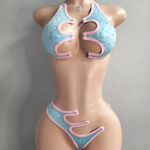 Può includere: Un set bikini azzurro con finiture rosa e strass. La parte superiore e inferiore presentano esclusivi design ritagliati. Il bikini è esposto su un manichino.