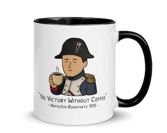 May include: White ceramic mug with a black interior and handle. The mug features a cartoon illustration of Napoleon Bonaparte holding a coffee cup, with the quote "No Victory Without Coffee" and the name "Napoléon Bonaparte 1815".